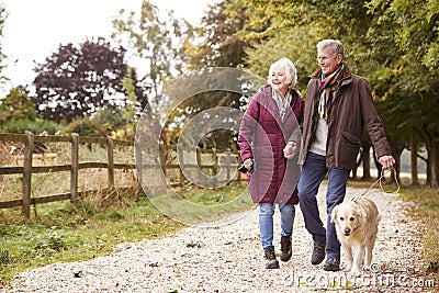 Active Senior Couple On Autumn Walk With Dog On Path Through Countryside Stock Photo