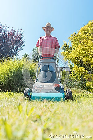 Active senior man smiling while using a grass cutting machine in the garden Stock Photo