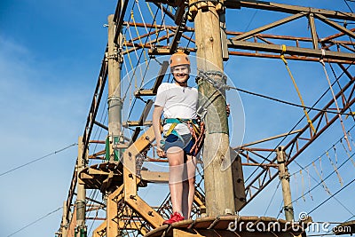 Active sporty kid in helmet doing activity in adventure park with all climbing equipment. Active children climb on the trees Stock Photo