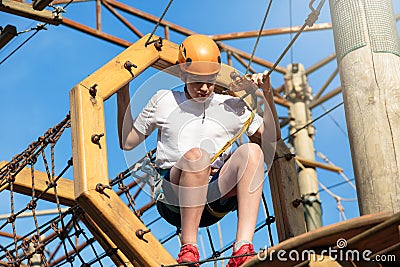 Active sporty kid in helmet doing activity in adventure park with all climbing equipment. Active children climb on the trees Stock Photo