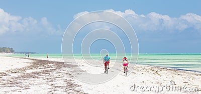 Active sporty tourist couple cycling down picture perfect white sand tropical beach of Paje, Zanzibar, Tanzania. Editorial Stock Photo