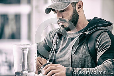 Active strong bearded man in cap and hoodie making protein shake beverage after heavy sport training fitness workout Stock Photo