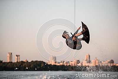 active strong man rider holds rope and skilfully making extreme jump showing trick on wakeboard. Stock Photo