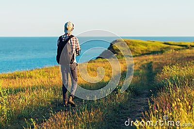 Active tourist, a man with a briefcase in nature, a hipster in a cap walks along a path on a green hill, against the background of Stock Photo