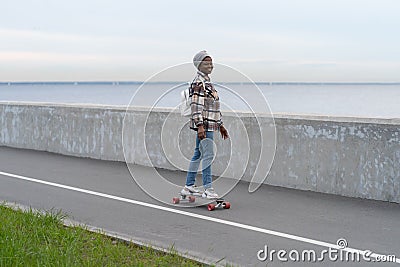 Active urban lifestyle: african girl riding longboard at seaside road. Smiling woman on skateboard Stock Photo