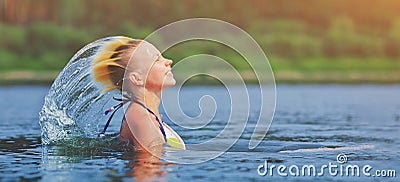 Active young blonde woman waving hair splashing water in river. Beautiful healthy lady relax and laughing, raising head out of the Stock Photo