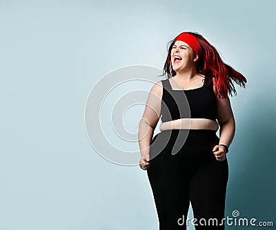 Active young plus-size woman with flowing red hair in black sport top and leggings shouting with laughter and delight Stock Photo