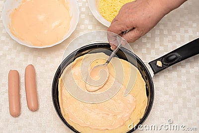 Adding sauce on the raw dough on black pan for homemade pizza by senior woman. Other ingredients are on the table. Top Stock Photo