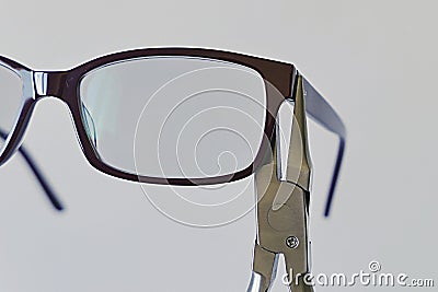 Adjusting inclination of temples on simple plastic eyeglass frame with steel chain nose pliers. Stock Photo