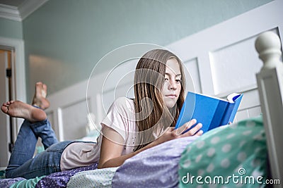 Adolescent teen girl reading a book while lying in bed at home in her bedroom. Lifestyle and learning photo Stock Photo