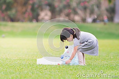 Adorable Asian girl is helping to collect plastic bottles on the lawn. Cute kid carrying garbage bags in the green lawn. Stock Photo