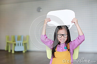 Adorable Asian little girl holding empty blank speech bubble to say something in the classroom with smiling and looking straight Stock Photo