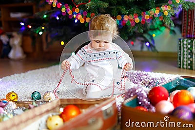 Adorable baby girl holding colorful lights garland in cute hands. Little child in festive clothes decorating Christmas Stock Photo