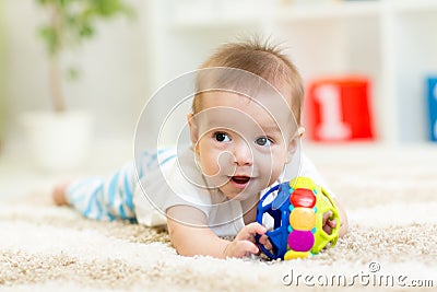 Adorable baby having fun with toy on cozy rug. Happy cheerful kid playing on the floor Stock Photo