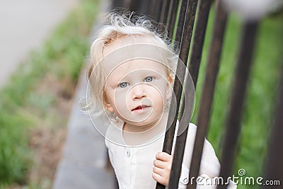 Adorable blomde baby girl is walking outdoors near the fence Stock Photo