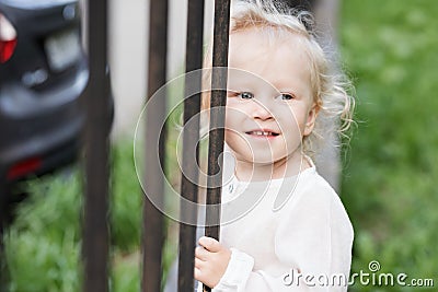 Adorable blomde baby girl is walking outdoors near the fence Stock Photo