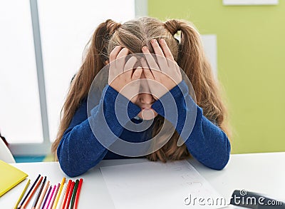 Adorable blonde girl student stressed covering face with hands at classroom Stock Photo