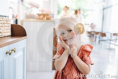 Adorable blonde little girl holding cookie on a stick, smiling at the camera. Stock Photo