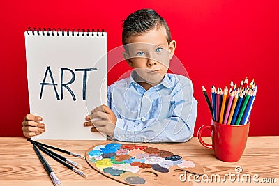 Adorable caucasian kid painter sitting at art studio holding art word depressed and worry for distress, crying angry and afraid Stock Photo