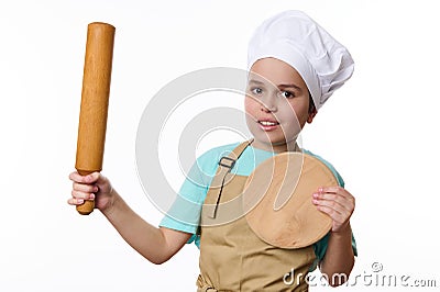 Adorable child boy, in chef's hat and apron, posing with a rolling pin and wooden cutting board, over white Stock Photo