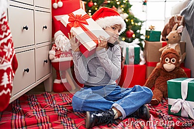 Adorable chinese girl hearing gift sound sitting on floor by christmas tree at home Stock Photo