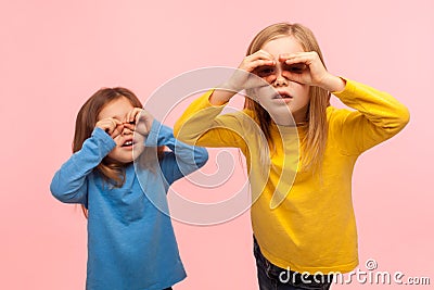 Adorable, curious, nosy two little girls looking through fingers imitating binoculars, exploring world Stock Photo