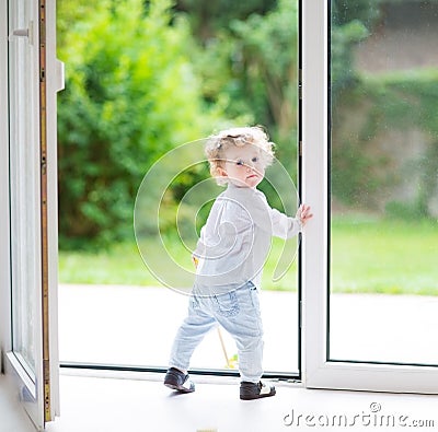 Adorable curly baby girl at big glass door to the garden Stock Photo