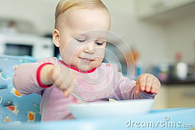 Adorable cute caucasian blond toddler boy eating tasty vegetable soup in chair at kithcen indoor. Mother feeding baby healthy food Stock Photo