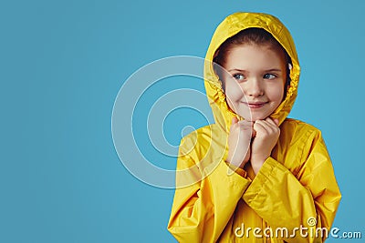 Girl kid wears yellow waterproof raincoat, keeps hands together under chin Stock Photo