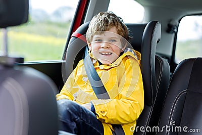 Adorable cute preschool kid boy sitting in car in yellow rain coat. Stock Photo