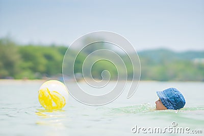 Adorable girl in blue hat swim in ocean near beach. Play with ye Stock Photo