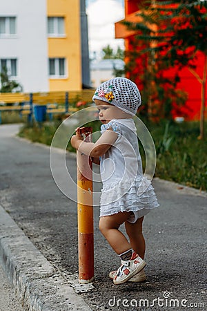 Adorable girl having fun on summer day. a little girl stands on the transition path and clings to the fence, pipe Stock Photo