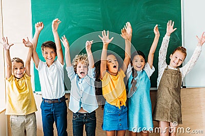 adorable happy schoolchildren with raised hands standing in front of Stock Photo