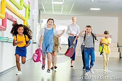 adorable happy schoolchildren running by school corridor together with teacher Stock Photo