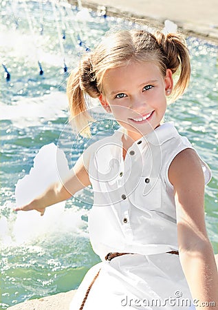 Adorable happy smiling little girl child sitting near the fountain Stock Photo