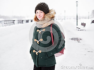 Adorable happy young redhead woman in green parka hat having fun at snowy winter exploring river pier Stock Photo