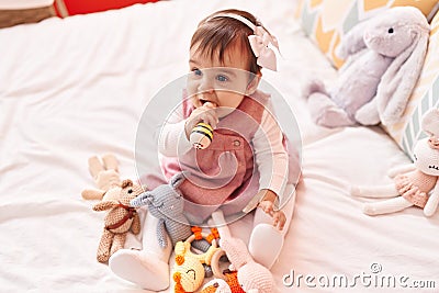 Adorable hispanic baby bitting maraca sitting on bed at bedroom Stock Photo