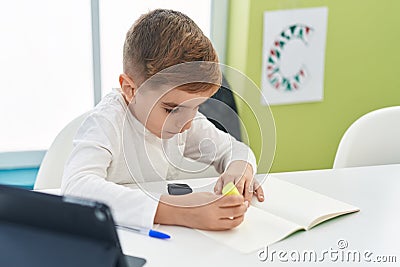 Adorable hispanic boy student using touchpad underlining on notebook at classroom Stock Photo