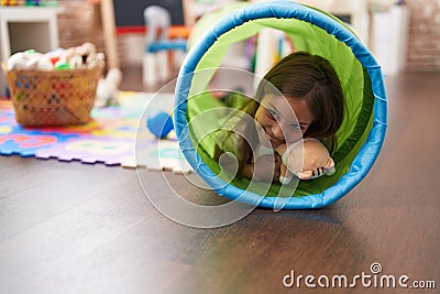 Adorable hispanic girl crawling inside tunnel toy at kindergarten Stock Photo