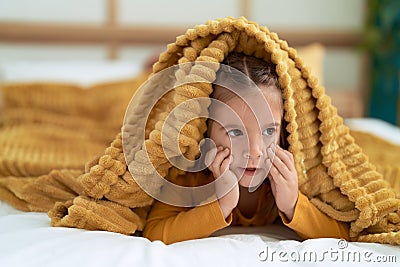 Adorable hispanic girl lying on bed covering with bedsheet at bedroom Stock Photo