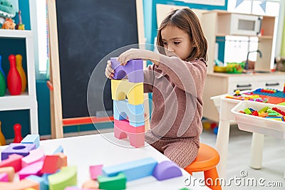 Adorable hispanic girl playing with construction blocks sitting on chair at kindergarten Stock Photo