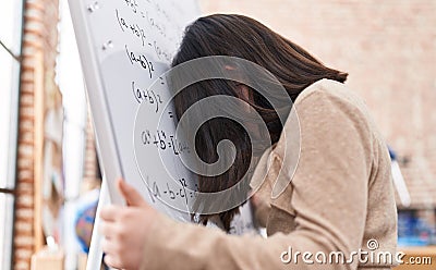 Adorable hispanic girl student solving maths exercise stressed with head on chalkboard at classroom Stock Photo