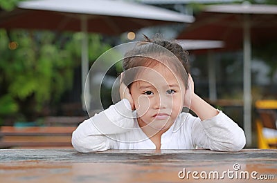 Adorable little Asian child girl expressed disappointment or displeasure on the wood table with looking camera Stock Photo
