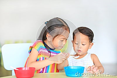 Adorable little Asian sister and her little brother eating cereal with cornflakes and milk together and friendly on the table. Stock Photo