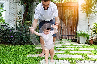 Adorable little baby daughter practice and learning walking that first time toddler girl walk on grass by father holding hands and Stock Photo