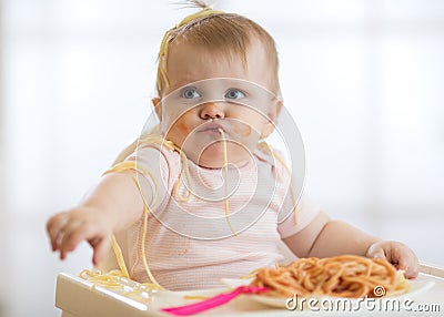 Adorable little baby one year eating pasta indoor. Funny toddler child with spaghetti. Cute kid and healthy food. Stock Photo