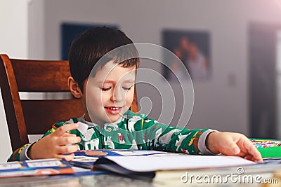 Adorable little boy reading book before going to sleep. Happy kid dressed in pajamas reads a story and amuses himself. Cute boy l Stock Photo