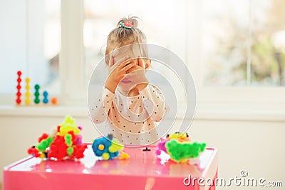 Adorable little cheerful girl playing cuckoo and close the face with hands, in kindergarten or preschool. Creative games for kids Stock Photo