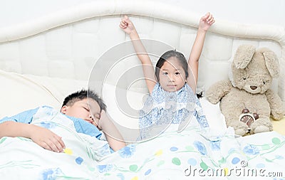 Adorable little cute girl awaked up in her bed and brother sleep Stock Photo