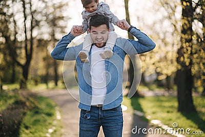 Adorable little daughter sitting on dad`s neck and laughing. Young father walk with his cute daughter in the park Stock Photo